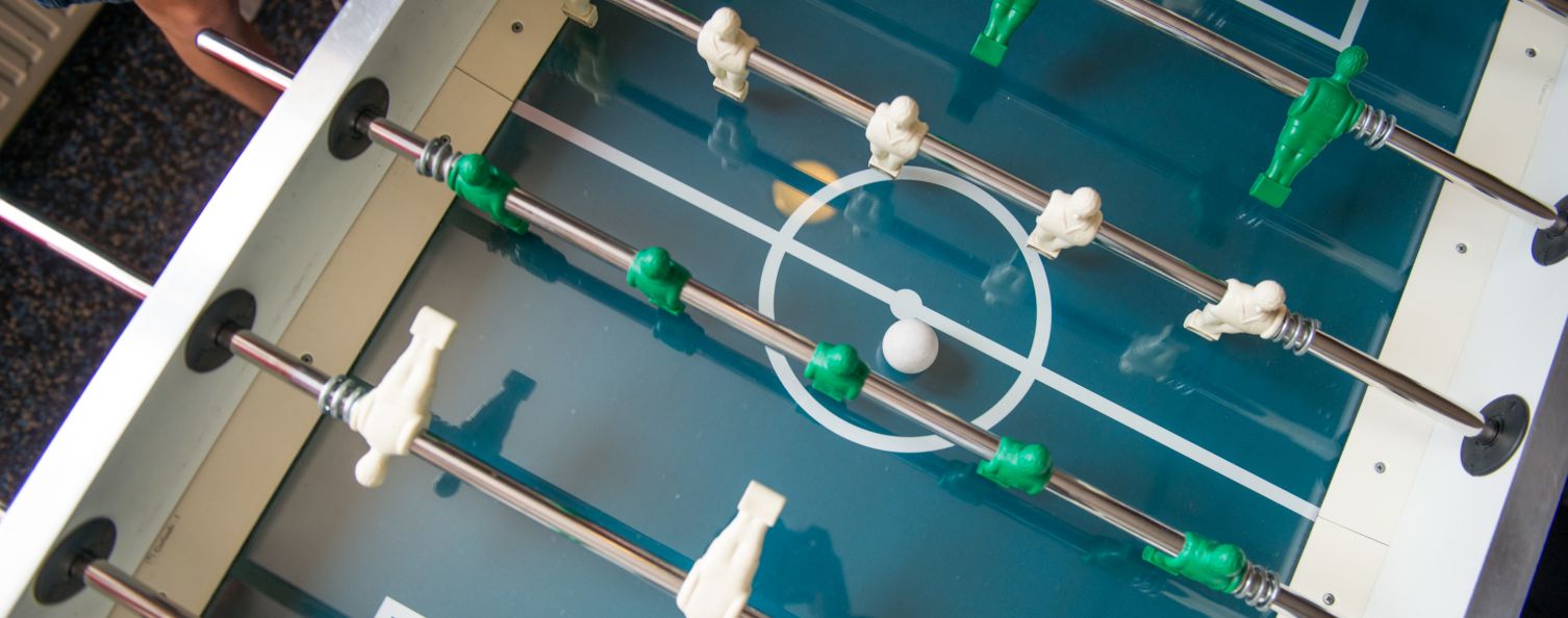 Draufsicht eines Kickertisches mit weißen und grünen Spielfiguren